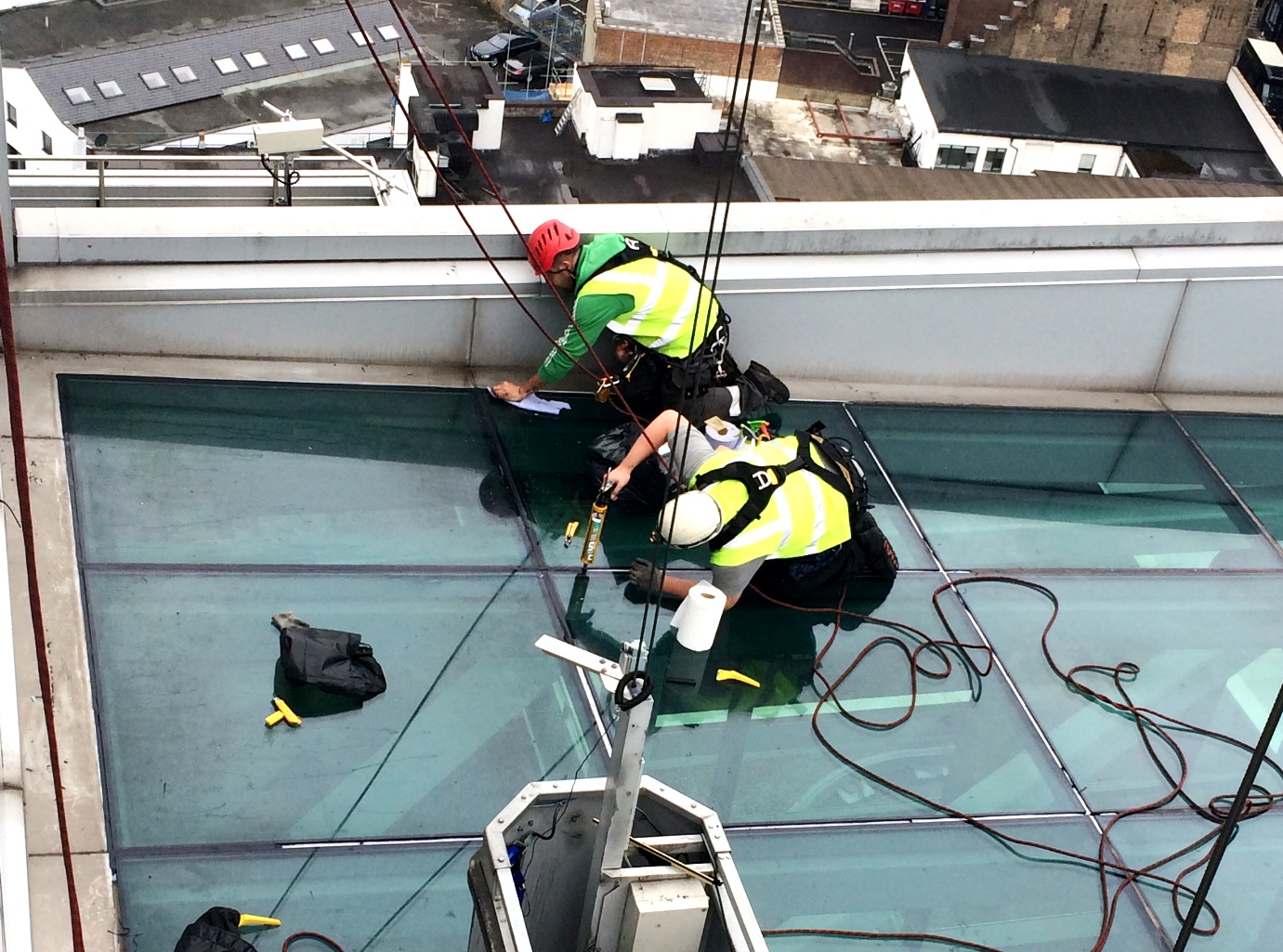 two men working to seal a glass pane on a glass roof